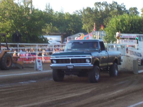 1994 Ford F-150 - A lifted green Ford pickup truck competes in an event on a dirt track, with spectators in the background.