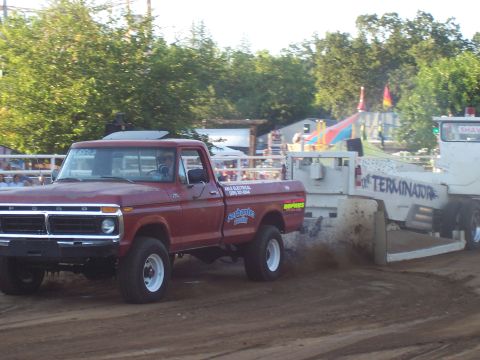 1994 Ford F-150 - A red pickup truck competes in a pull event, dragging a trailer with "TERMINATOR" written on its side.