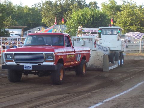 1994 Ford F-150 - A red Ford pickup truck, likely from the late 1970s, competes in a pull event, dragging a heavy sled across the dirt track.