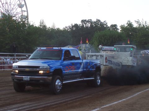1994 Ford F-150 - A blue pickup truck competes in a pull event, with a sled emitting dark smoke behind it.