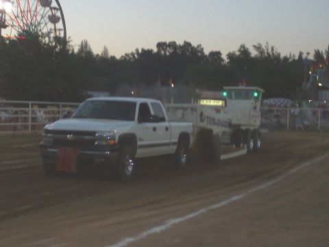 1994 Ford F-150 - White Chevrolet Silverado truck pulls a sled at a dirt track event with a Ferris wheel visible.