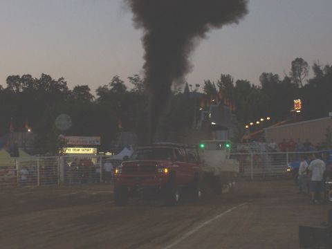 1994 Ford F-150 - A red pickup truck is seen pulling a trailer while emitting a large plume of black smoke, possibly during a competition.