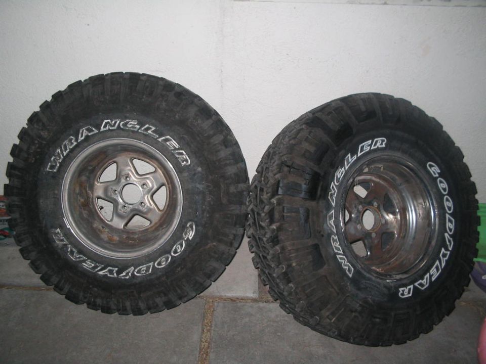 Two Goodyear Wrangler mud tires on five-spoke aluminum wheels against a garage wall