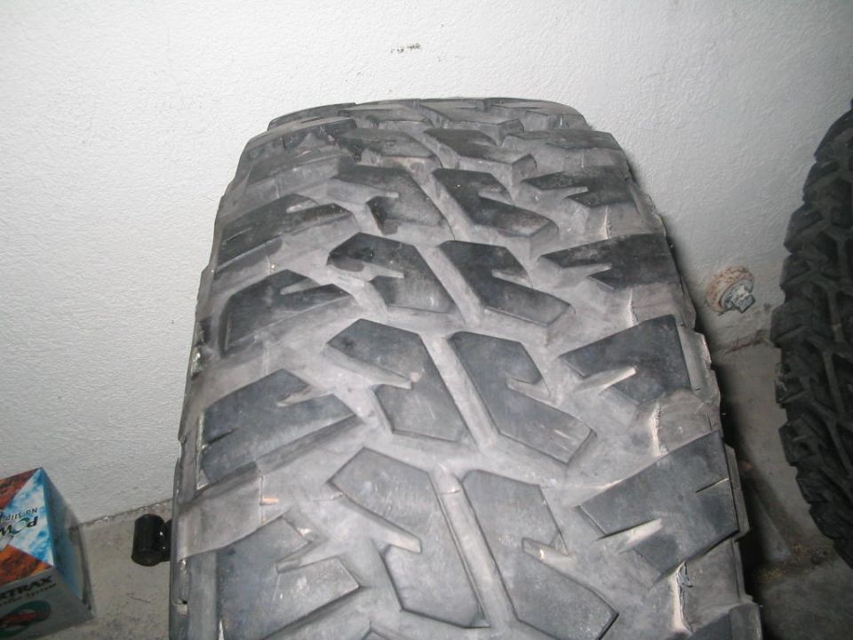 Close-up of aggressive mud-terrain tire tread standing against a white garage wall