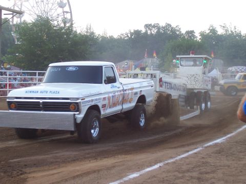 1994 Ford F-150 - A white Ford pickup truck competes in a pull event, dragging a trailer across a dirt track.