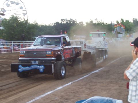 1994 Ford F-150 - Modified pickup truck competes in a pull event, kicking up dust as it tows a trailer.