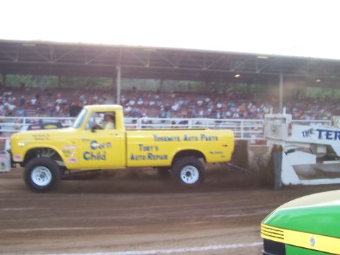 1994 Ford F-150 - A yellow pickup truck competes in a pull event, with spectators in the background.