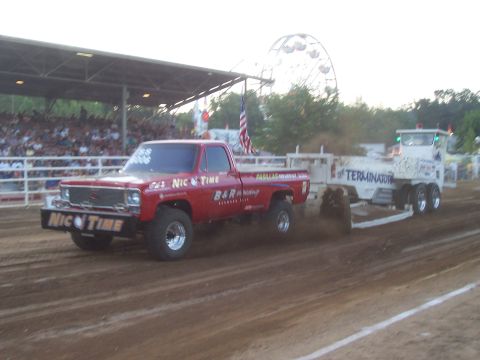 1994 Ford F-150 - A red pickup truck competes in a pull event, dragging a trailer across a dirt track.