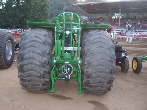 1994 Ford F-150 - A green tractor puller is viewed from the rear, its enormous tires and competition roll cage at an outdoor event.