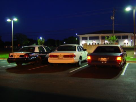 1988 Ford LTD Crown Victoria - Three sedans are parked in a lot at night, with a police car on the left.
