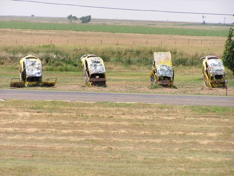 1993 Ford Taurus - Four derelict yellow vehicles are positioned upright in a grassy field, suggesting a unique roadside attraction or art installation.