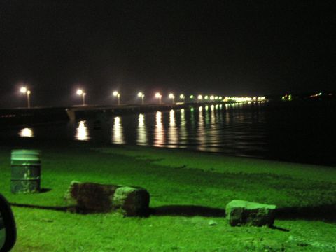 1993 Ford Taurus - A long pier with lights stretches over the water at night, with a grassy embankment in the foreground.