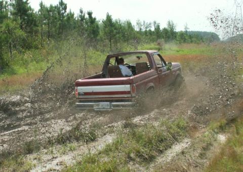 1988 Ford Bronco - 1988 Ford Bronco navigates a muddy trail, sending mud flying.