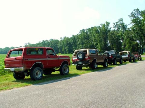 1988 Ford Bronco - Multiple Ford Broncos are lined up on the side of a road under a clear sky.