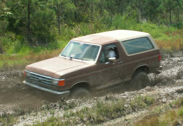 Brown 1988 Ford Bronco driving through mud