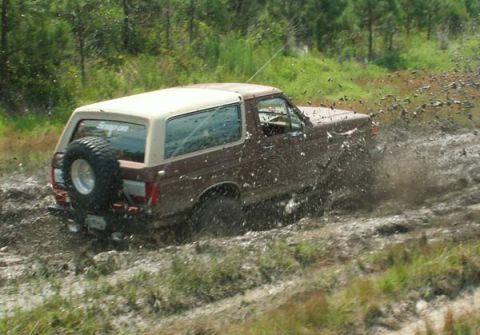 1988 Ford Bronco - Ford Bronco navigating a muddy trail, kicking up a large spray.