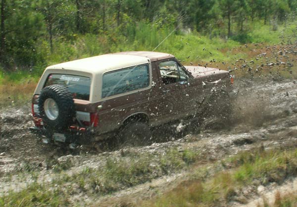 1988 Ford Bronco driving through mud, splashing water and dirt