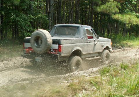 1988 Ford Bronco - A Ford Bronco navigates a muddy trail, kicking up dirt and water.