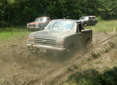 1988 Ford Bronco - Three Ford trucks, including a Bronco, navigate a muddy trail.