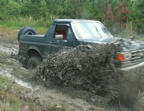 1988 Ford Bronco - This Ford Bronco is navigating a muddy trail, kicking up a large spray of mud.