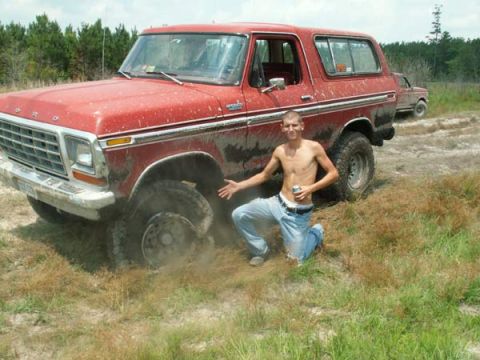1988 Ford Bronco - A man poses next to a mud-covered Ford Bronco that appears to be stuck in the dirt, with another vehicle visible in the distance.