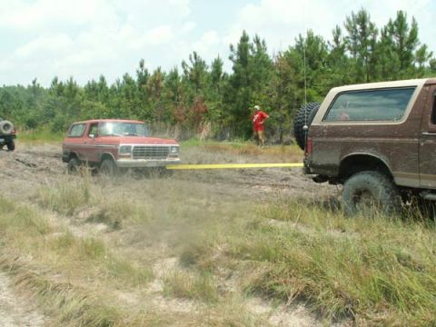 1988 Ford Bronco - Two Ford Broncos navigate a muddy terrain, with one appearing to be stuck and towed by the other.