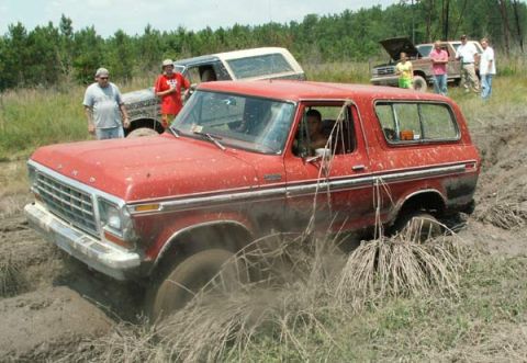 1988 Ford Bronco - A red SUV is stuck in the mud while other vehicles and people are present in the background.