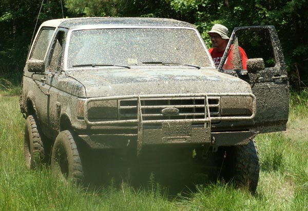 Muddy SUV with door open, person in hat and red shirt standing by it