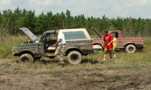 1988 Ford Bronco - Two trucks are stuck in the mud with their hoods open.