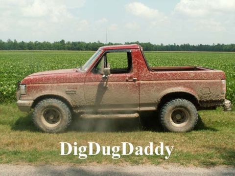 1988 Ford Bronco - This red Ford Bronco is covered in mud and parked in a grassy field.