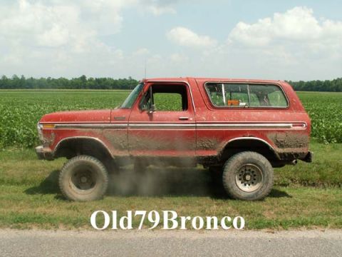 1988 Ford Bronco - Muddy red Ford Bronco parked on the side of a dirt road next to a field.
