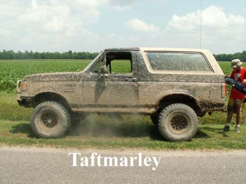 1988 Ford Bronco - A person stands next to a heavily mud-covered SUV in a grassy field.