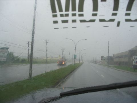 1986 Ford Bronco - Driving through heavy rain on a city street, with a truck visible in the distance.