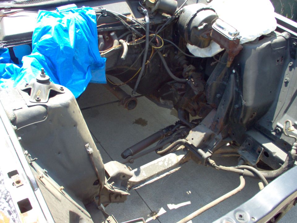 Empty rusty engine bay of a stripped classic car with blue tarp over the cowl