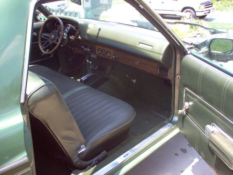 1970 Ford Ranchero - The interior of a green 1970 Ford Ranchero shows a bench seat, wood-grain dashboard accents, and a column shifter.