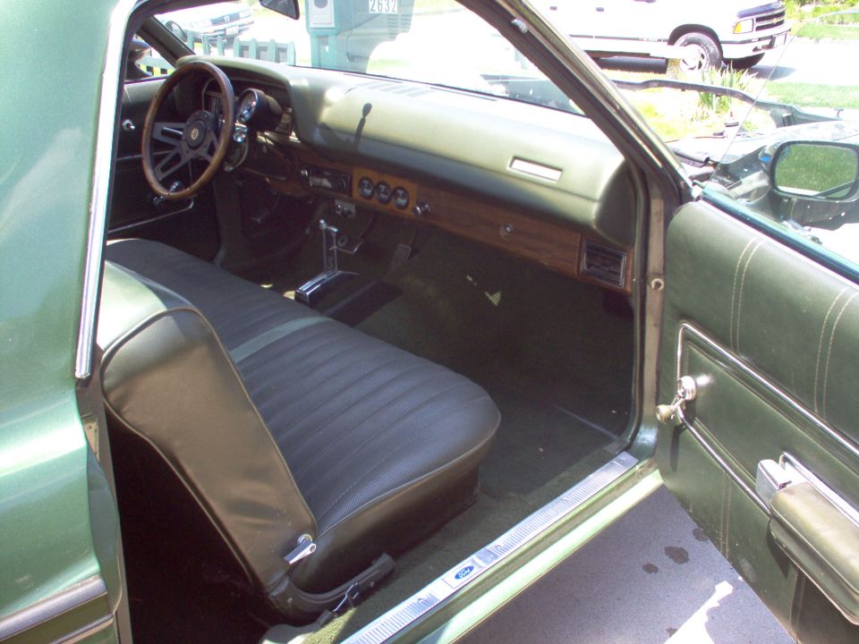 Green vinyl bench seat and woodgrain dash inside a 1970s Ford, passenger door open