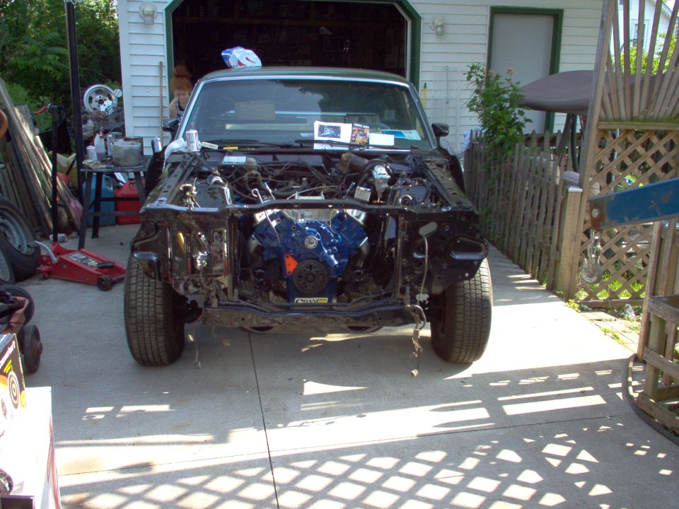 Project car front clip removed in driveway exposing blue Ford V8 engine
