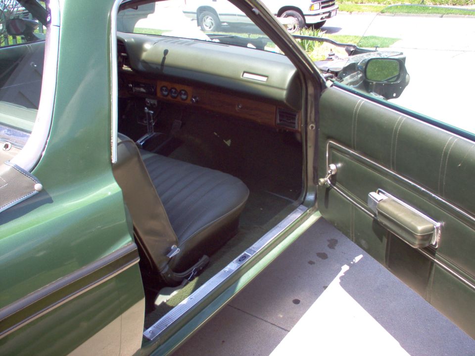 Open passenger door of a green classic car showing black vinyl bench seat and woodgrain dash