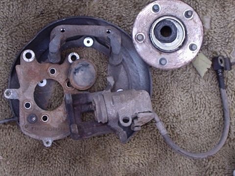 2000 Ford Taurus - Disassembled car brake components, including a caliper, rotor, and hub assembly, are laid out on a textured surface.