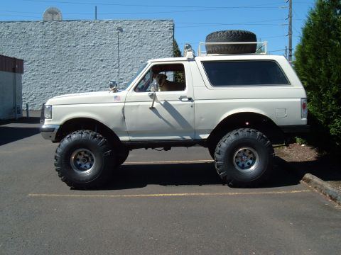 1989 Ford Bronco - Side view of a lifted 1989 Ford Bronco with oversized tires and a spare on the roof.