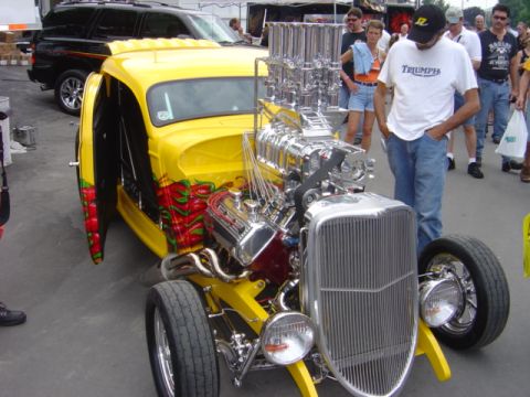 1998 Ford Taurus - A highly customized yellow hot rod with a prominent supercharger and flame graphics is displayed outdoors.