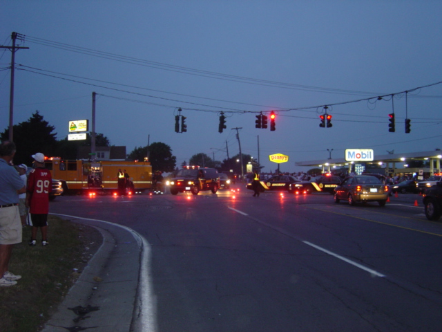 Traffic incident scene at dusk with a fire truck, police cars, and civilian vehicles at an intersection with traffic lights