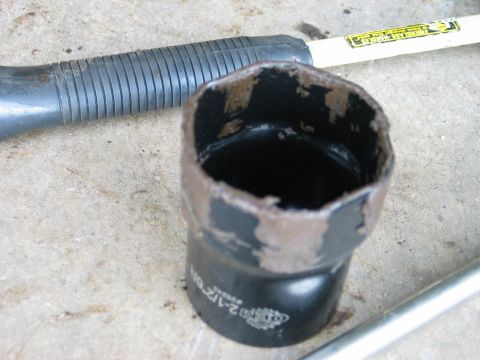1995 Ford Bronco - A black 2-1/2 inch exhaust pipe adapter or reducer coupling lying on a concrete floor, its upper edge torn and jagged from being cut, with…