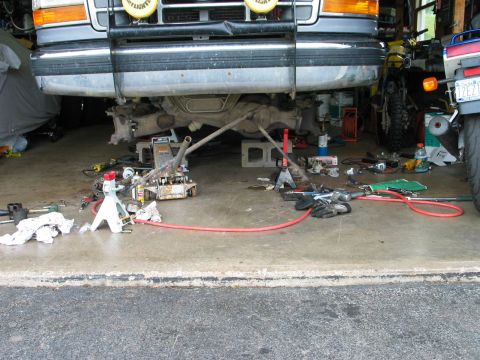 1995 Ford Bronco - Front-on view of a two-tone Ford truck raised on jack stands in a garage, shot low across the concrete floor to show the front axle, drives…