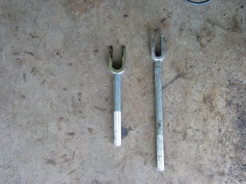 1995 Ford Bronco - Two pickle-fork tie-rod and ball-joint separators laid side by side on a stained concrete garage floor, shot from directly overhead. The le…