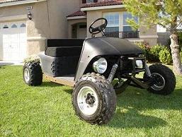 1990 Ford Bronco - small black off-road go-kart buggy with knobby tires sits on a green lawn in front of a stucco home.