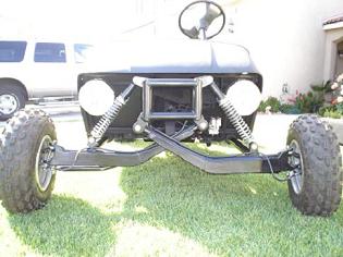 1990 Ford Bronco - black tubular sandrail-style buggy front end with coilover shocks and knobby tires sits on a grassy yard.