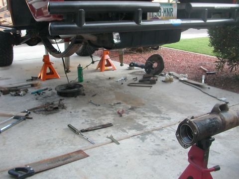 1984 Ford Bronco - The rear axle of a red SUV is disassembled, with parts and tools laid out on the concrete driveway.