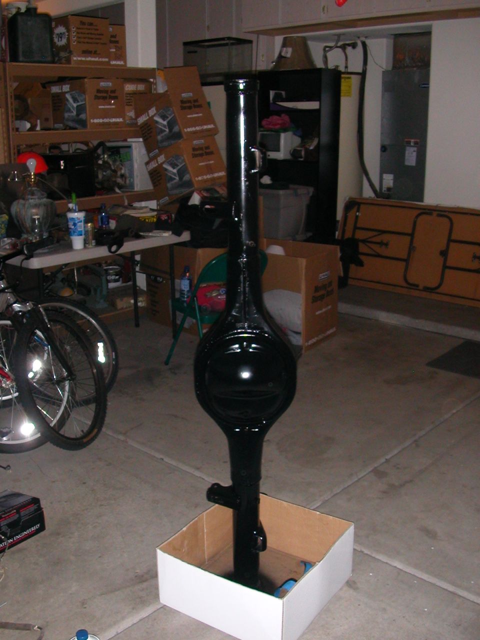Rear axle housing painted gloss black standing upright in a box to dry in a garage