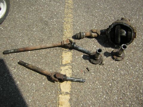 1995 Ford Bronco - Several automotive drivetrain components, including a differential and driveshafts, are displayed on a paved surface.